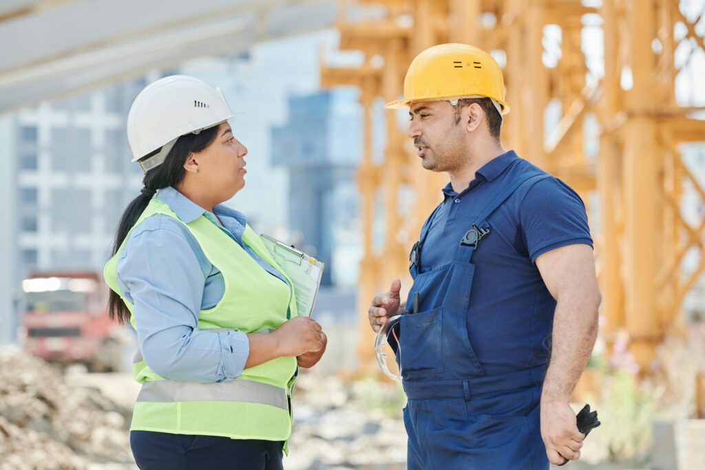 Two engineers wearing hard hats discuss project plans at a construction site.