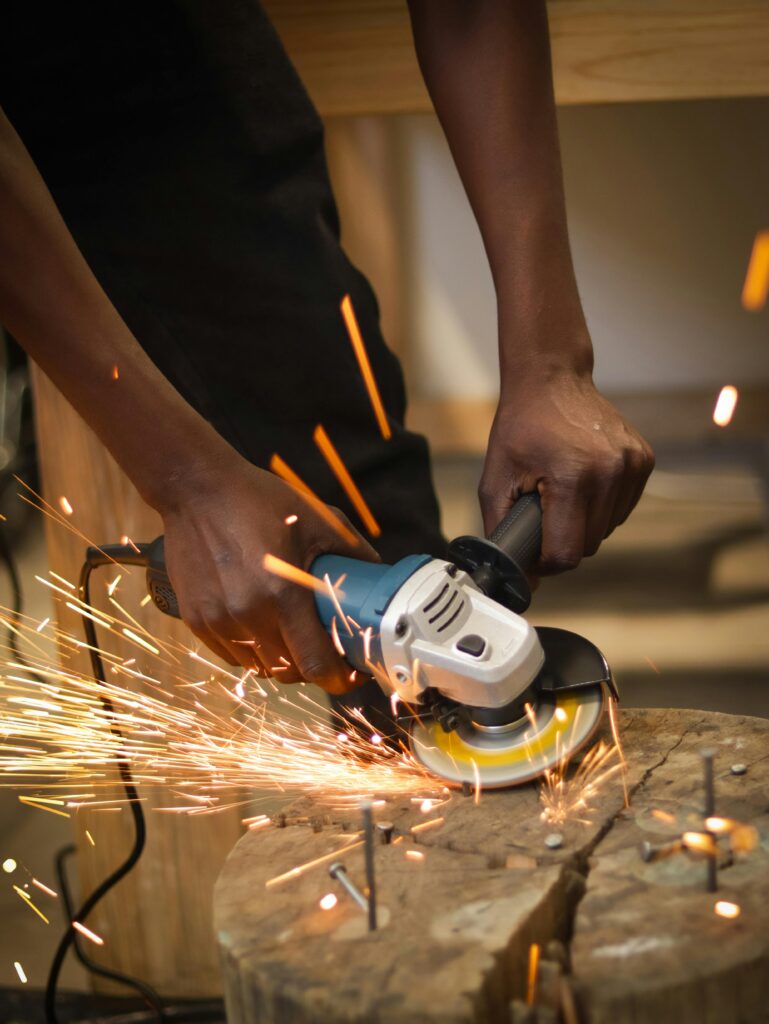 Close-up of hands using an angle grinder on wood with flying sparks.